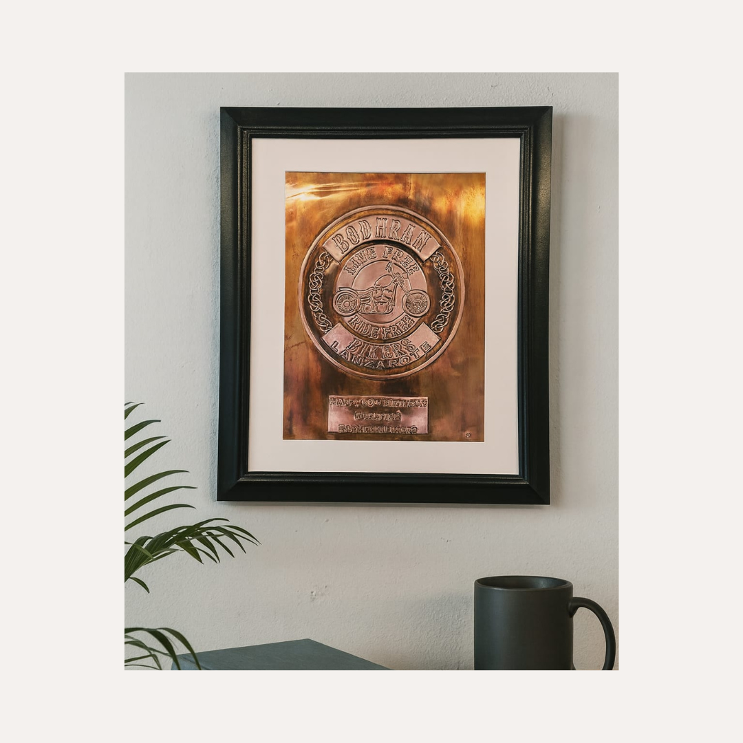 Framed metallic plaque on a wall with a plant and mug in the foreground