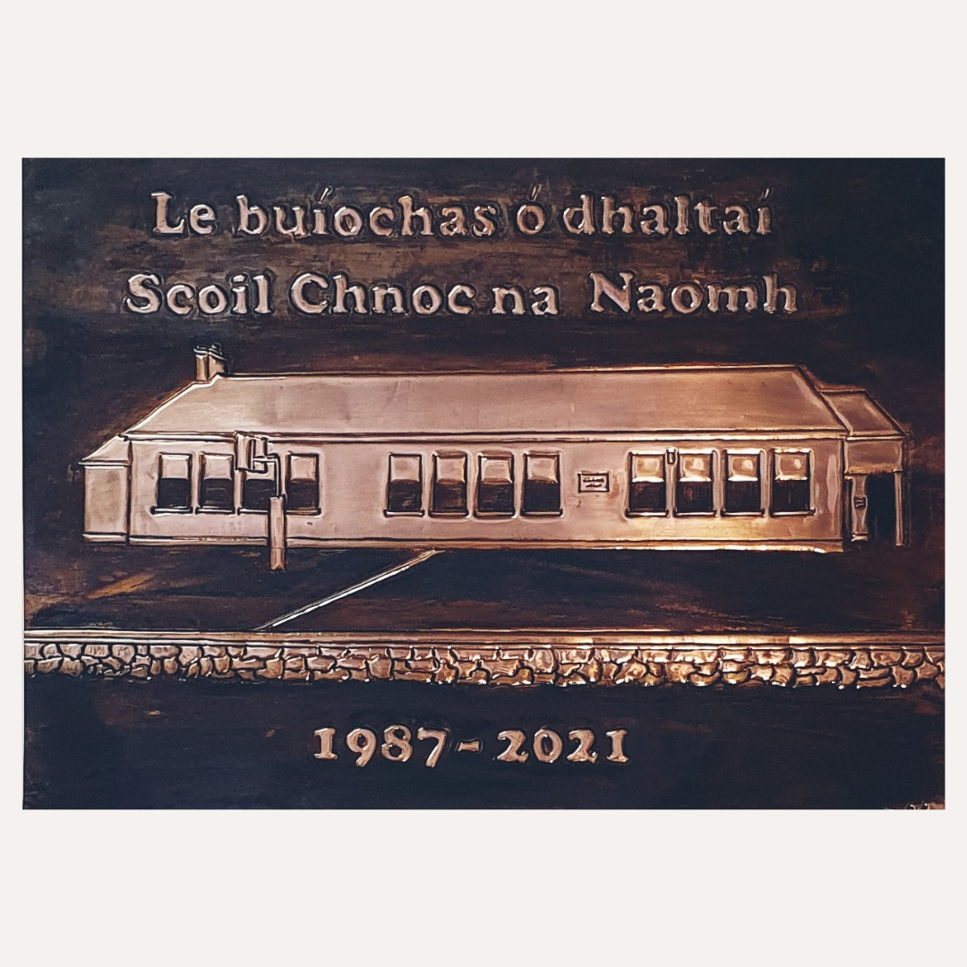Framed handcrafted copper school plaque featuring Scoil Chnoc na Naomh building with Irish inscription and engraved dates 1987–2021, presented in a wooden frame.