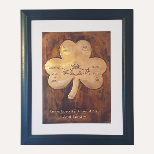 A framed copper plaque depicting a shamrock with engraved family names and a central Claddagh symbol, celebrating love, loyalty, friendship, and family.