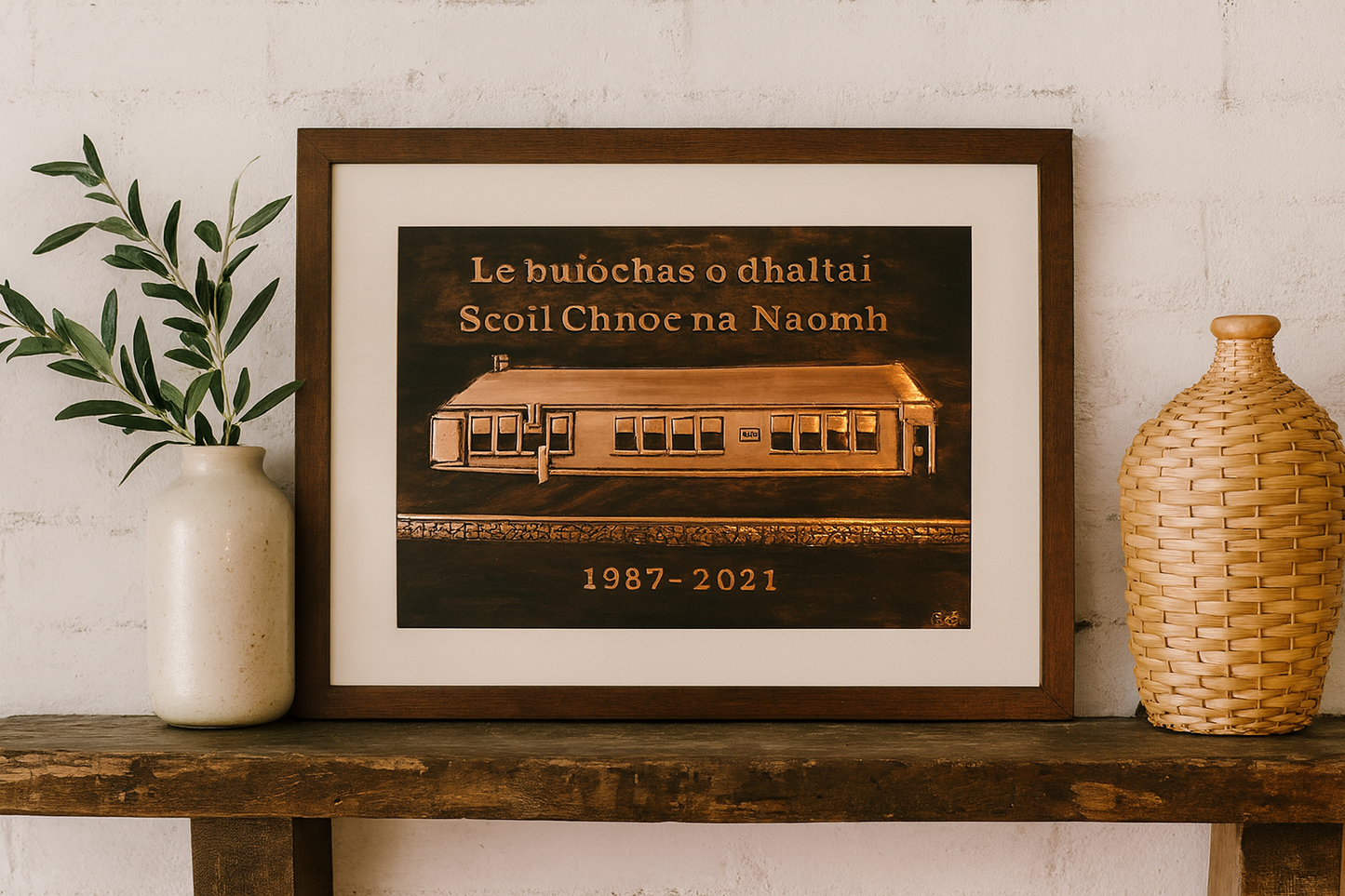 Handcrafted copper school commemorative plaque with Irish inscription, framed and placed on a wooden shelf with decorative accents in a modern home setting.