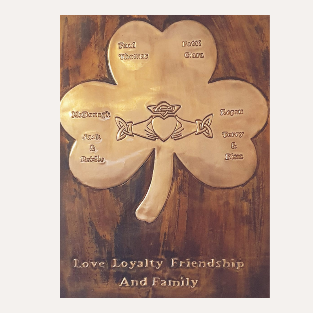 A framed copper plaque depicting a shamrock with engraved family names and a central Claddagh symbol, celebrating love, loyalty, friendship, and family.