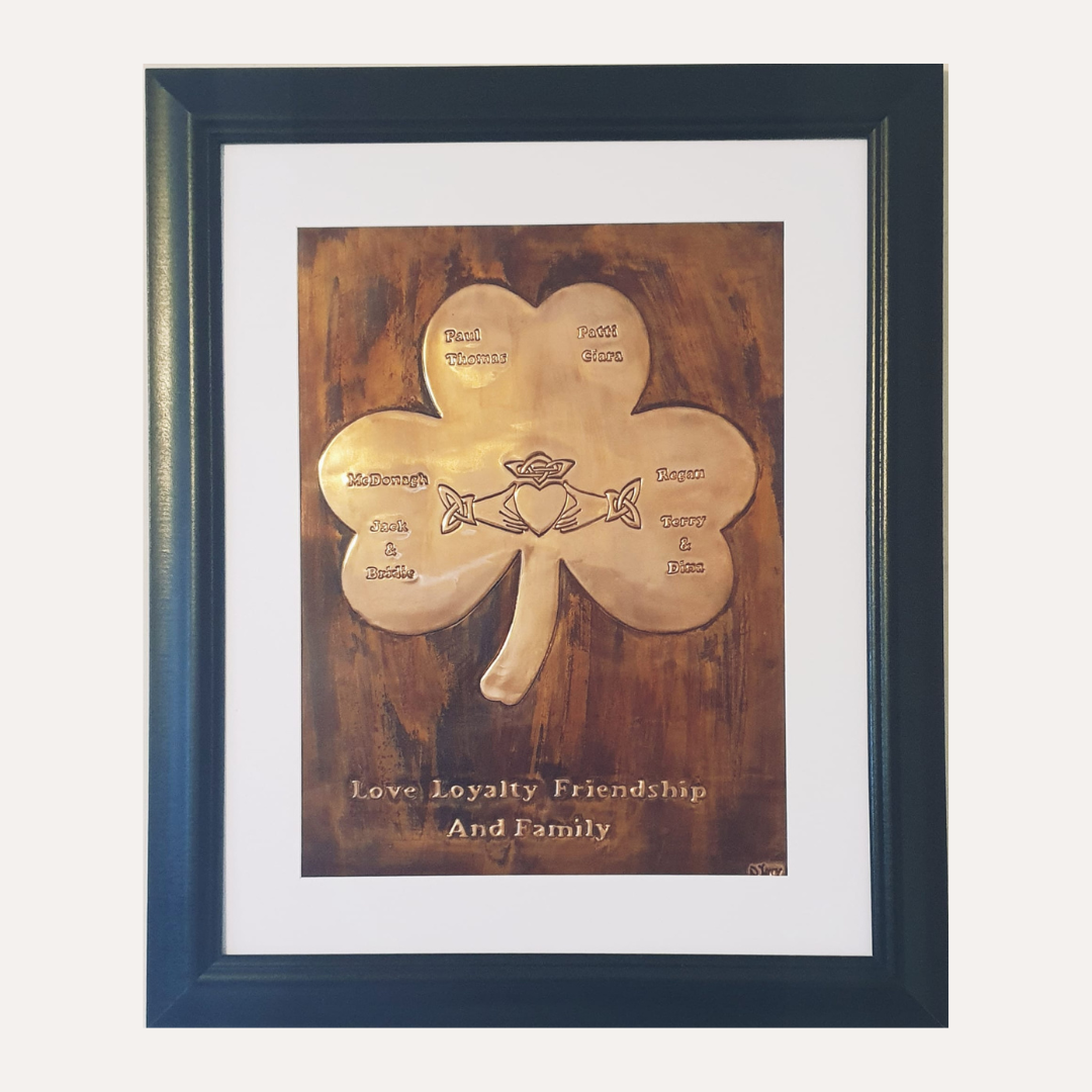 A framed copper plaque depicting a shamrock with engraved family names and a central Claddagh symbol, celebrating love, loyalty, friendship, and family.