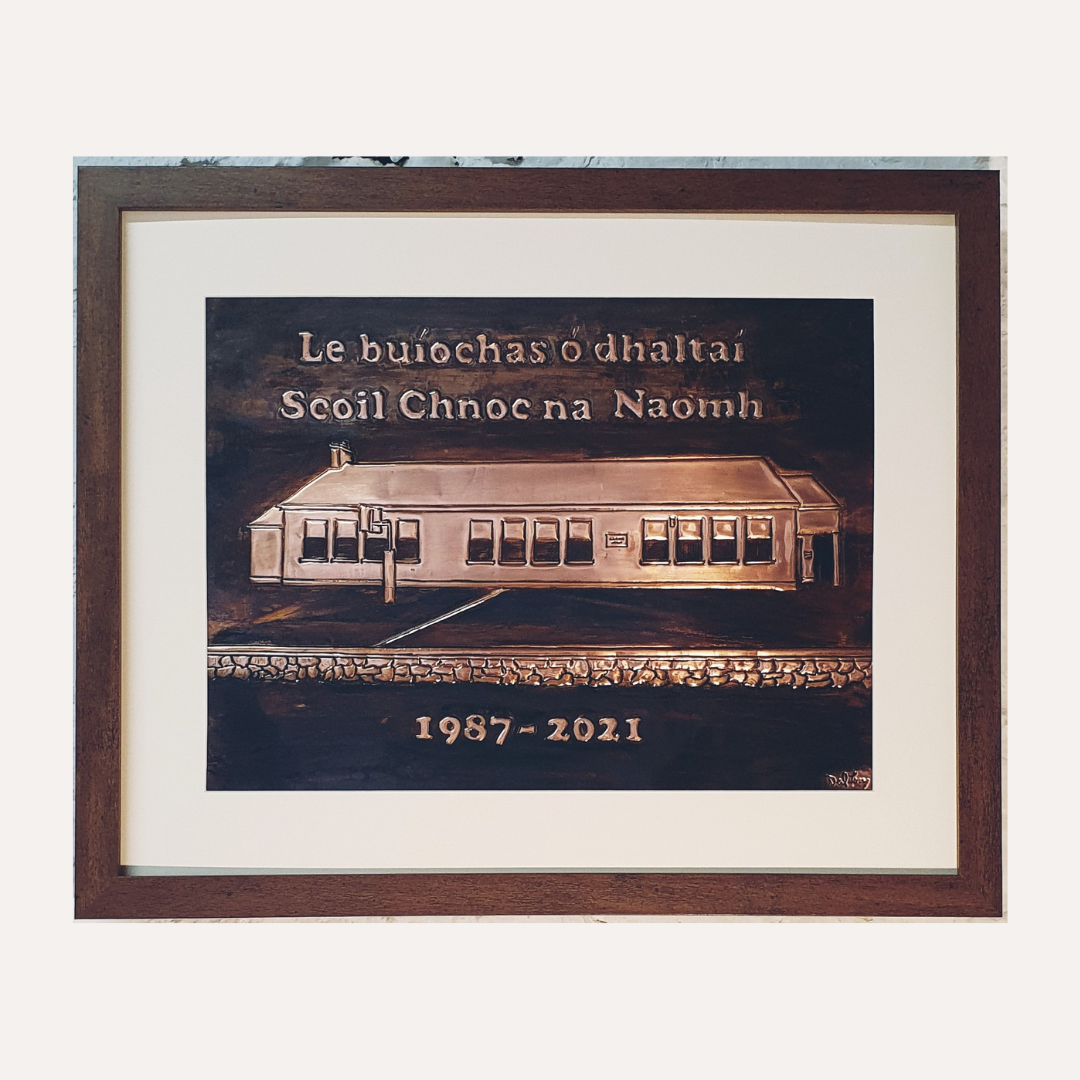 Framed handcrafted copper school plaque featuring Scoil Chnoc na Naomh building with Irish inscription and engraved dates 1987–2021, presented in a wooden frame.