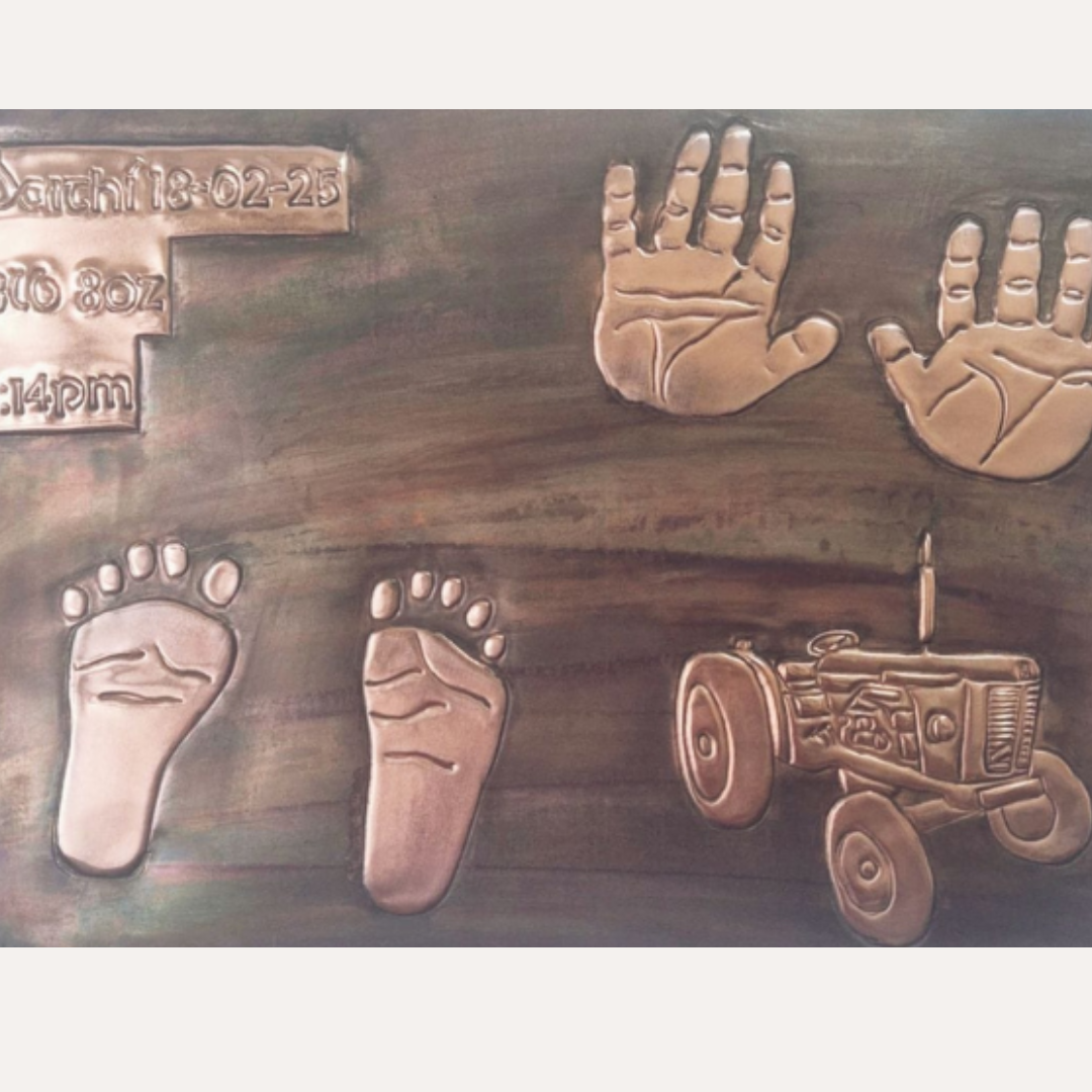 Handcrafted copper baby plaque with white frame showing handprints, footprints and birth details beside engraved tractor